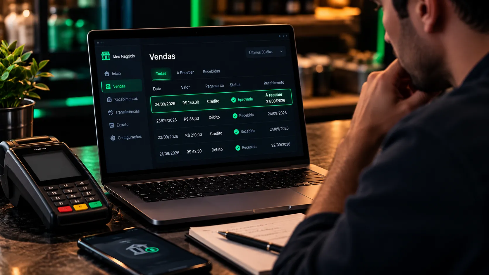 Comerciante consultando recebimentos de vendas em um notebook, com uma maquininha de cartão ao lado.